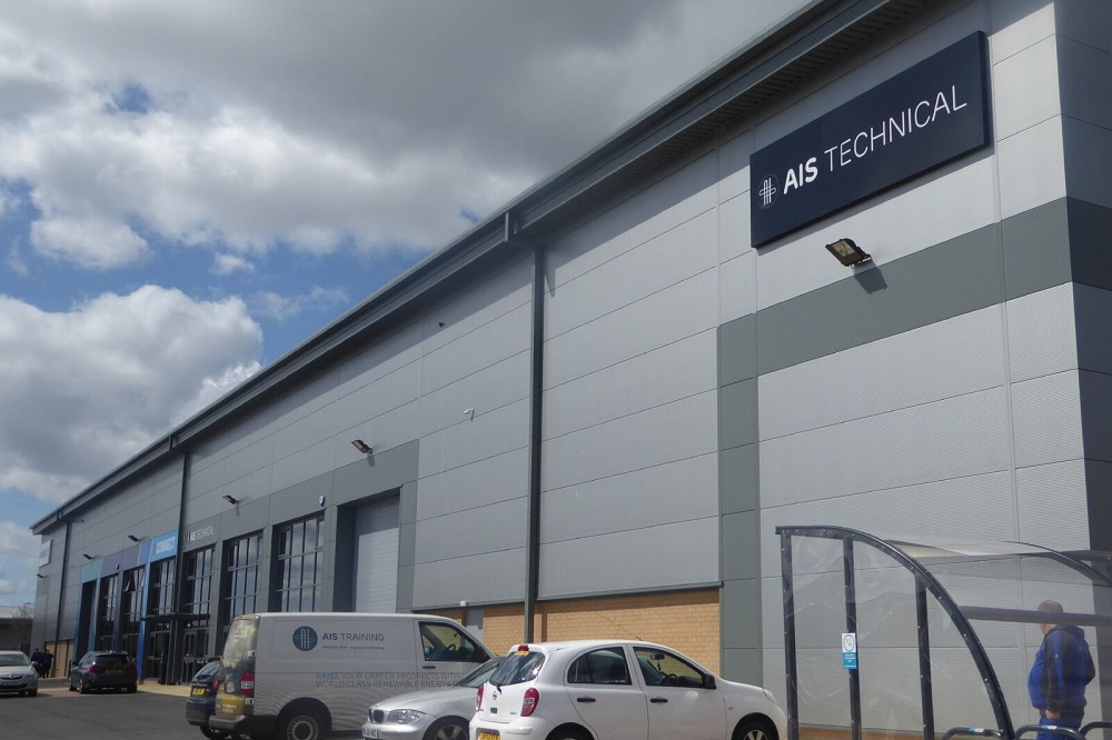 Outdoor view of AIS Technical building with parked cars in front. The structure has large doors and signs indicating the company's name. Cloudy sky overhead.