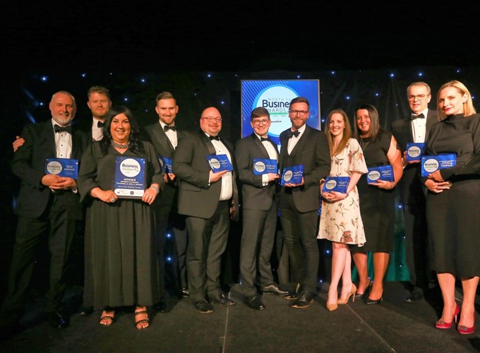 A group of people in formal attire holding awards, standing in front of a banner that reads 