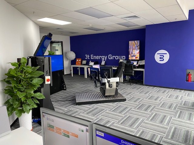 An office with a blue and white color scheme features the 3t Energy Group logo, several desks with computers, a plant, and specialized equipment in the foreground.