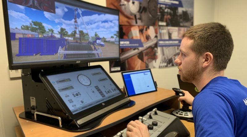 A person operates a machine simulator with multiple screens displaying controls and a simulated outdoor drilling scene.