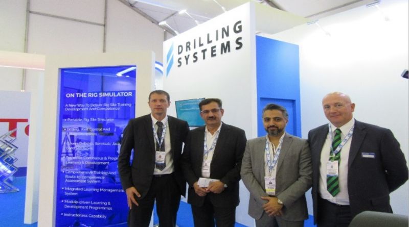 Four men in business attire stand in front of a Drilling Systems booth at a trade show.