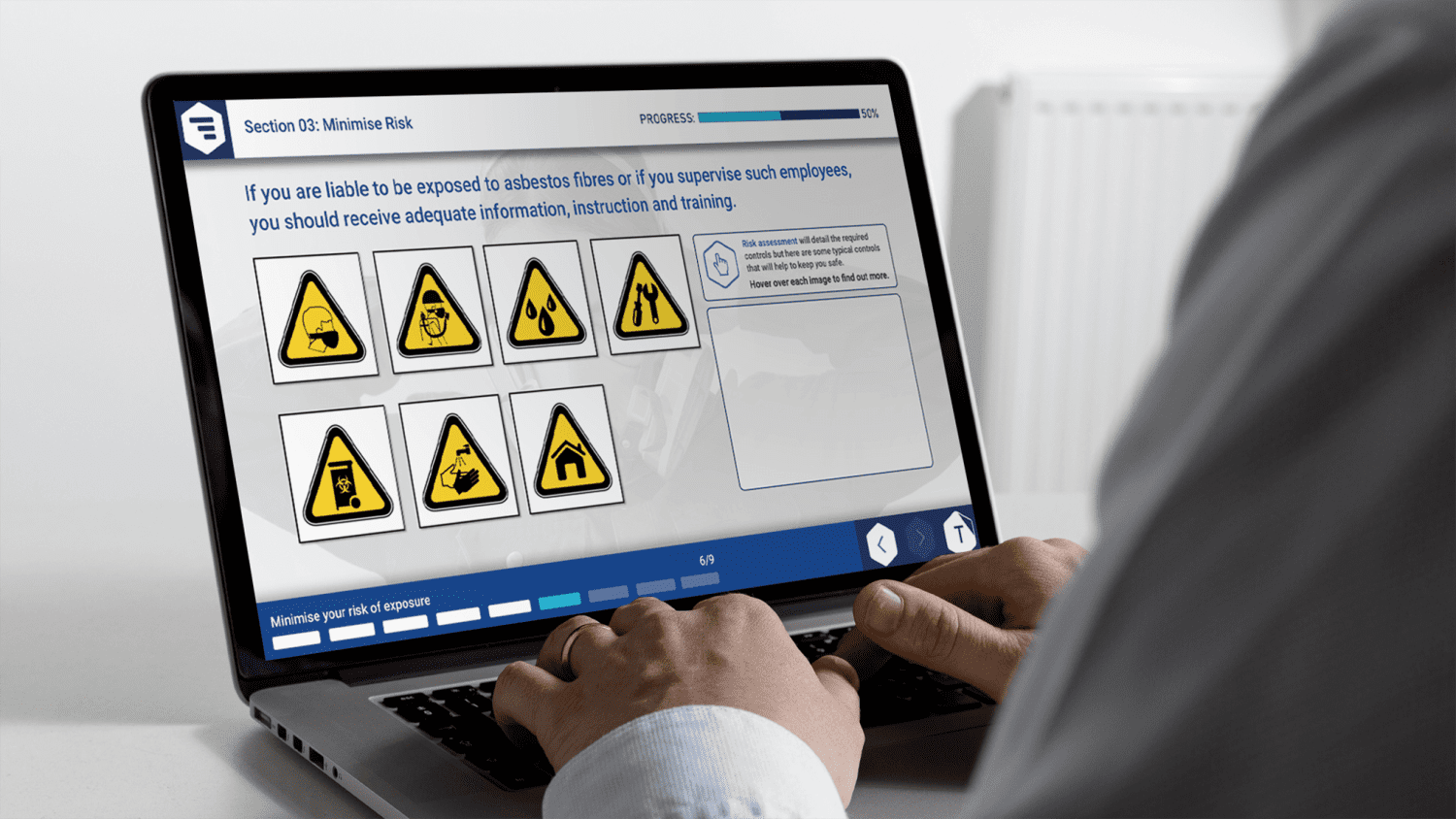 A person uses a laptop displaying a training module on minimizing asbestos risk with hazard symbols and instructional text on the screen.