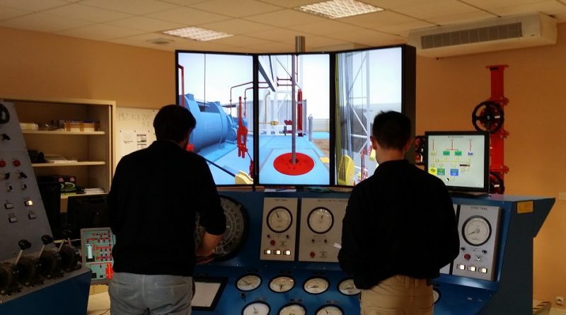 Two people operating a simulator with multiple screens and control panels in a control room setting.