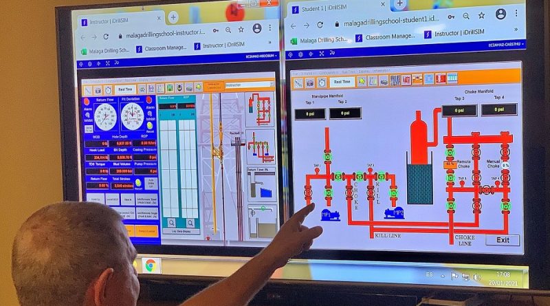 A person points at two computer screens displaying detailed diagrams and controls, seemingly related to a technical or industrial application.