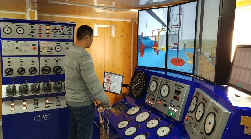 Person operating a training simulator for drilling systems, featuring multiple control panels and a digital display showing a drilling rig scenario.