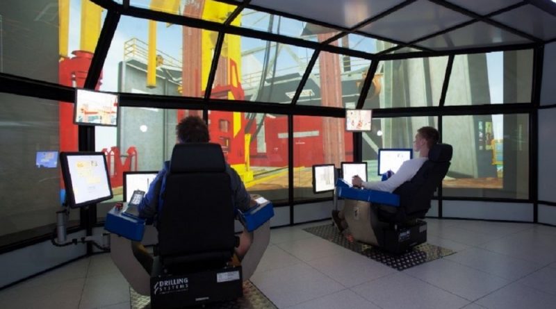 Two people operating simulators in a room with large screen displays showing an industrial environment, possibly for training purposes.