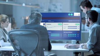 Four people in an office are sitting around a table, focusing on a digital screen displaying graphs and metrics.