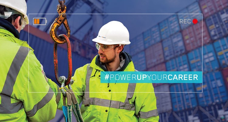 Two workers with safety gear and helmets handling a large hook in front of stacked shipping containers. Text overlay reads: 