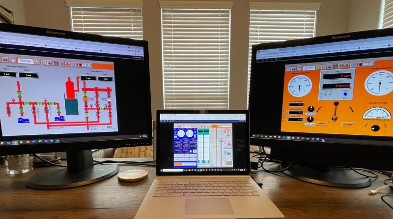 A desk with two large monitors displaying system control interfaces and a laptop in the center also showing a control interface. Three windows with closed blinds are in the background.