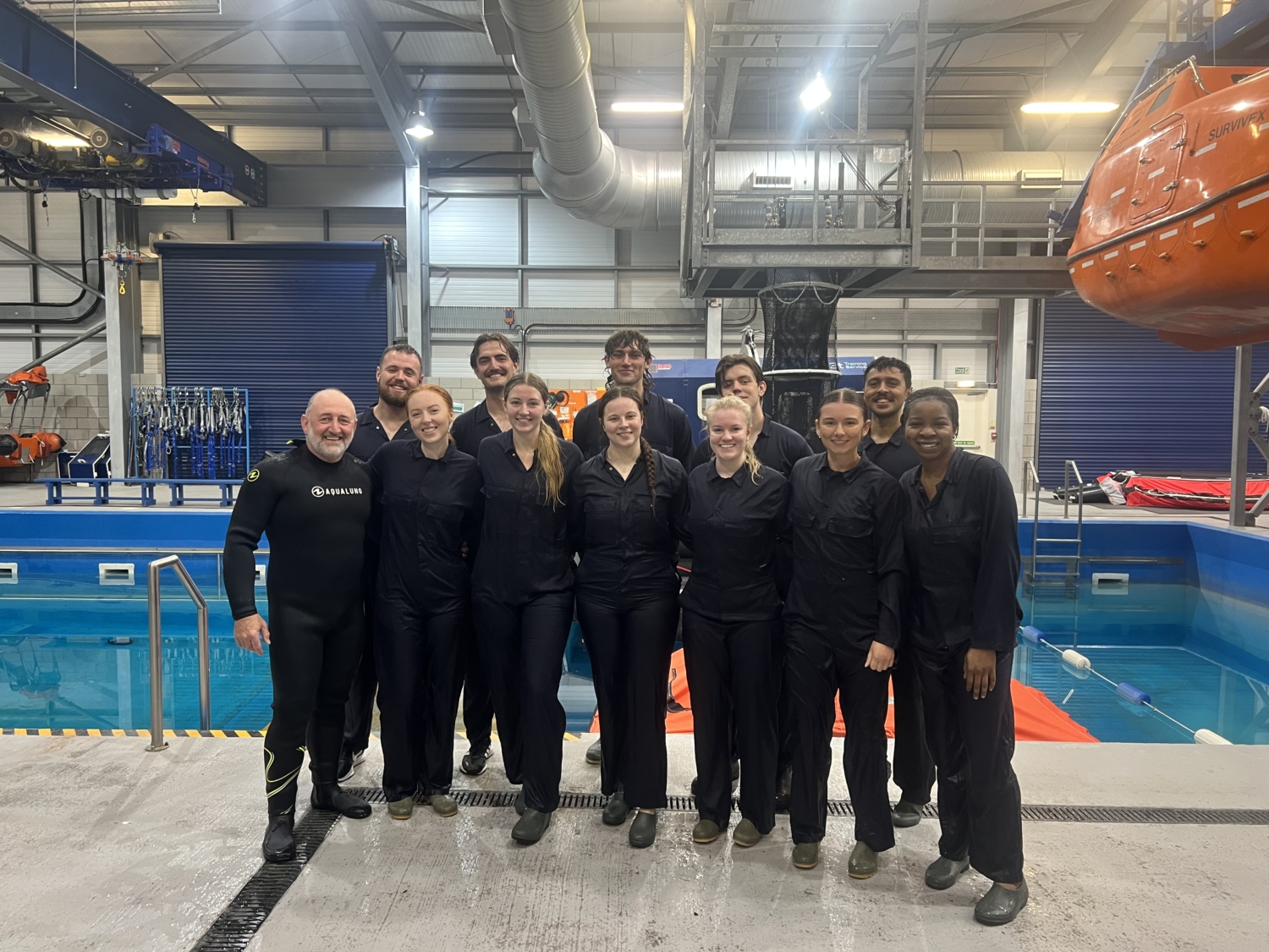 Un groupe de personnes vêtues de noir se tient ensemble dans une installation intérieure près d'une piscine et d'équipements de sécurité, posant pour une photo de groupe.