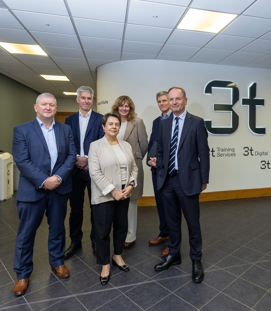 Six people in business attire stand in a tiled hallway next to a wall with 