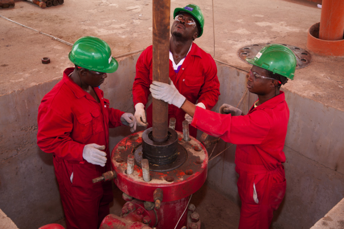 Three workers in red uniforms and green helmets are operating heavy machinery in an industrial setting.