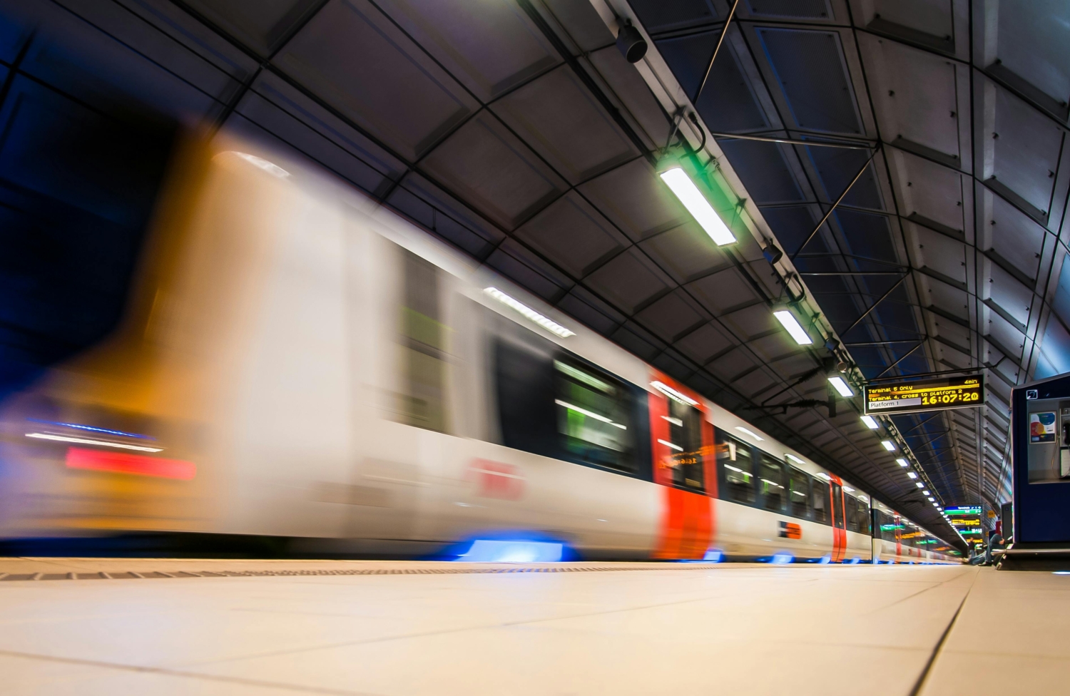 A fast-moving train passes through an underground station, with overhead signs visible. The image captures the motion blur of the train.